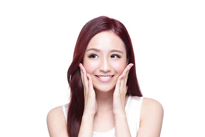 Smiling woman with red hair touching her cheeks against a white background