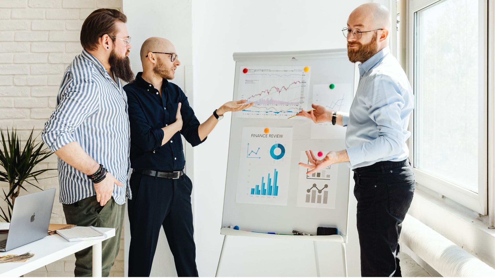 Three people discussing charts on a flip chart in a bright office room