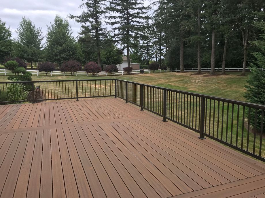 A wooden deck with a metal railing and trees in the background