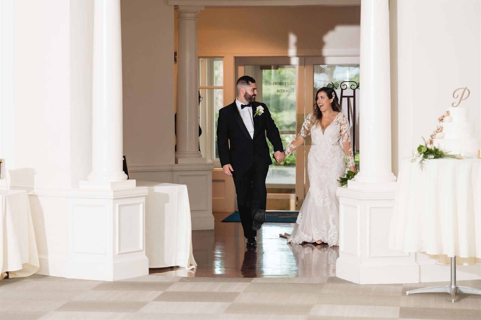 A bride and groom are walking through a hallway holding hands.