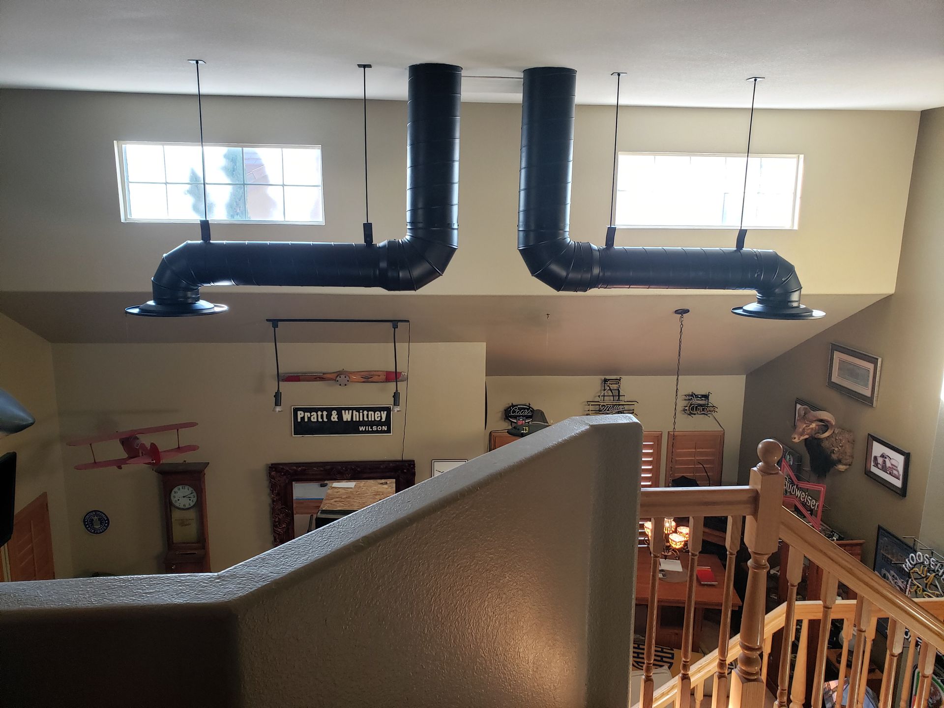 Open loft living room with black ventilation ducts and bright windows above a staircase.