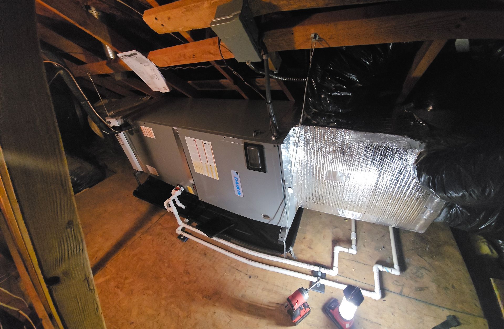 HVAC unit in attic with insulated ducts and exposed framing, lit by a flashlight