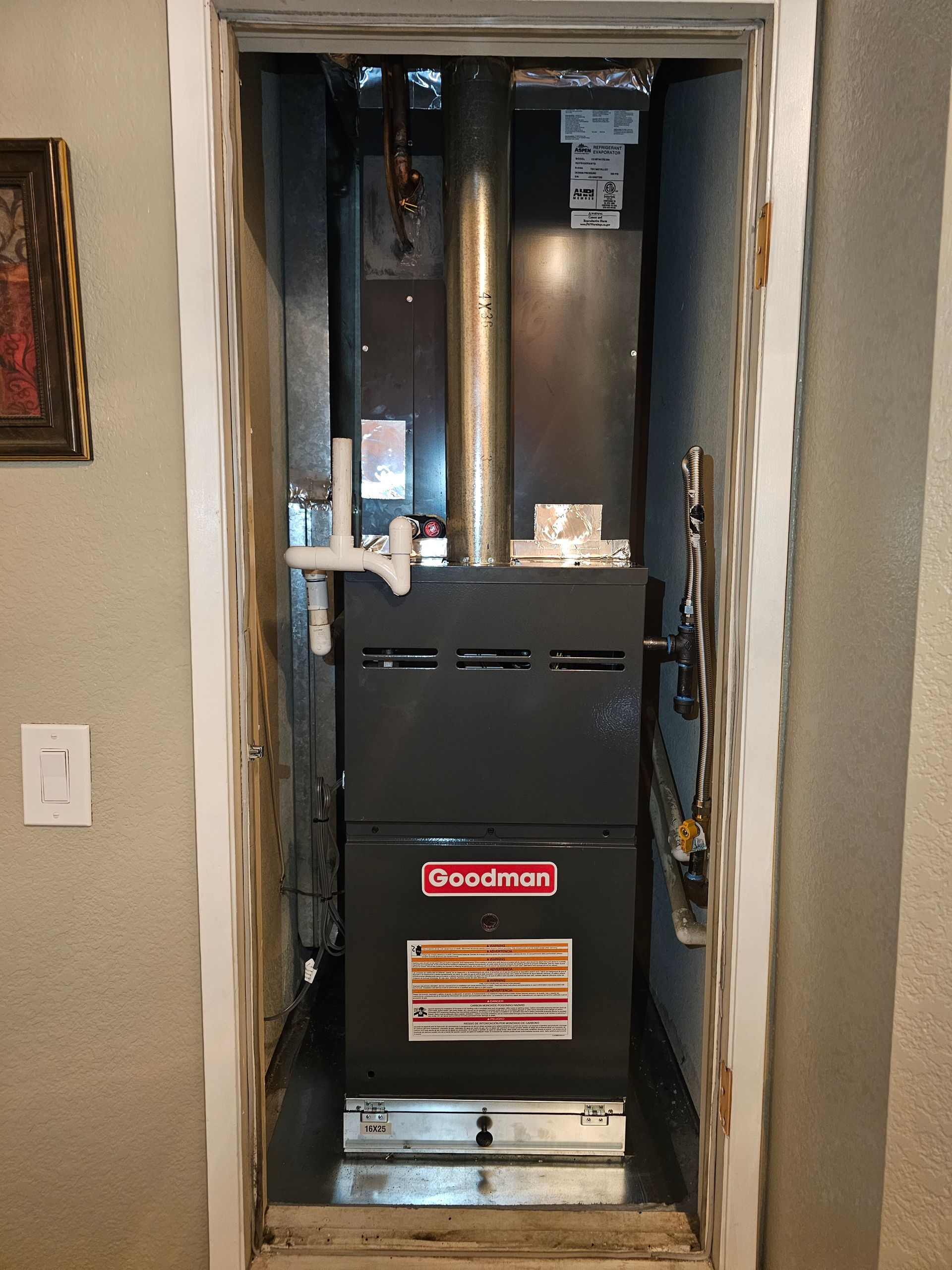 Open closet with a black Goodman furnace and exposed ductwork in a hallway wall opening