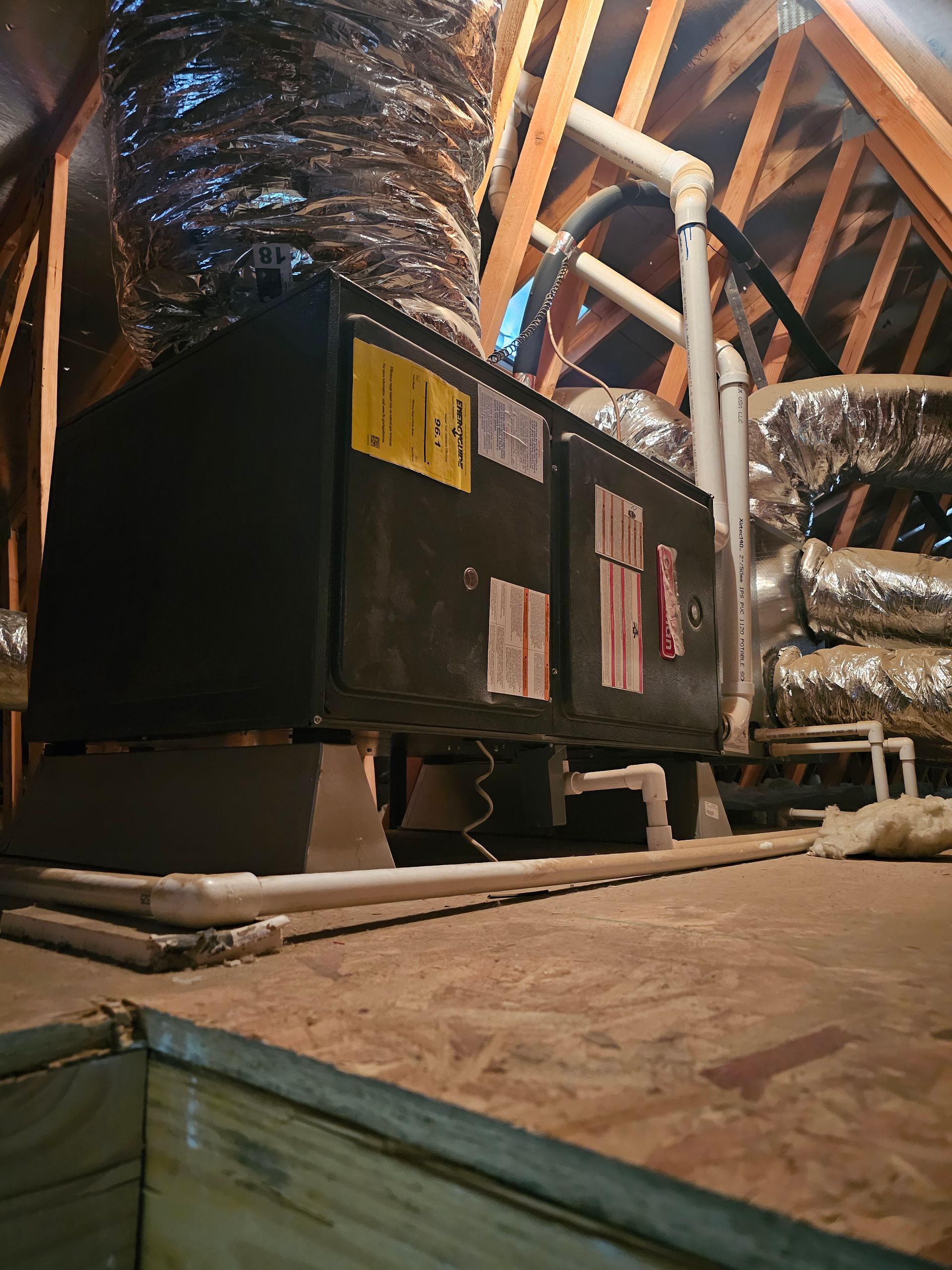 Black HVAC unit in an attic, surrounded by exposed ducts and wooden rafters