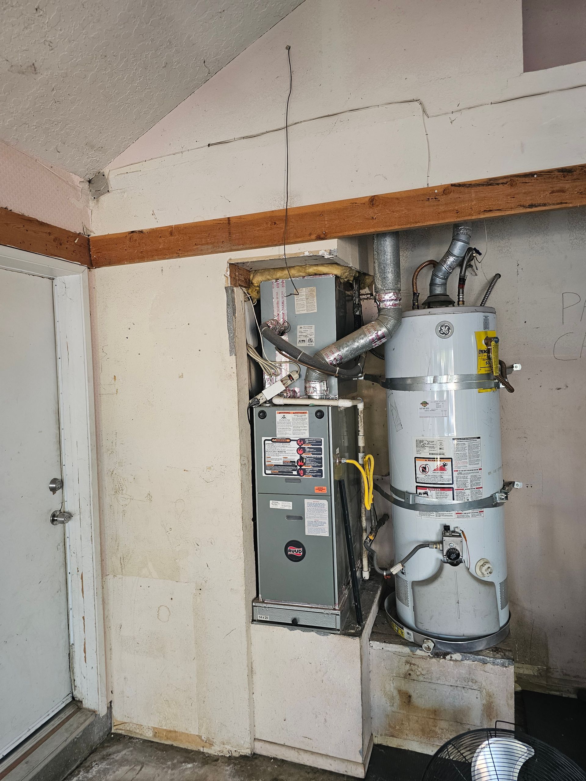 Electrical panel and water heater in a utility closet with exposed pipes and wiring.