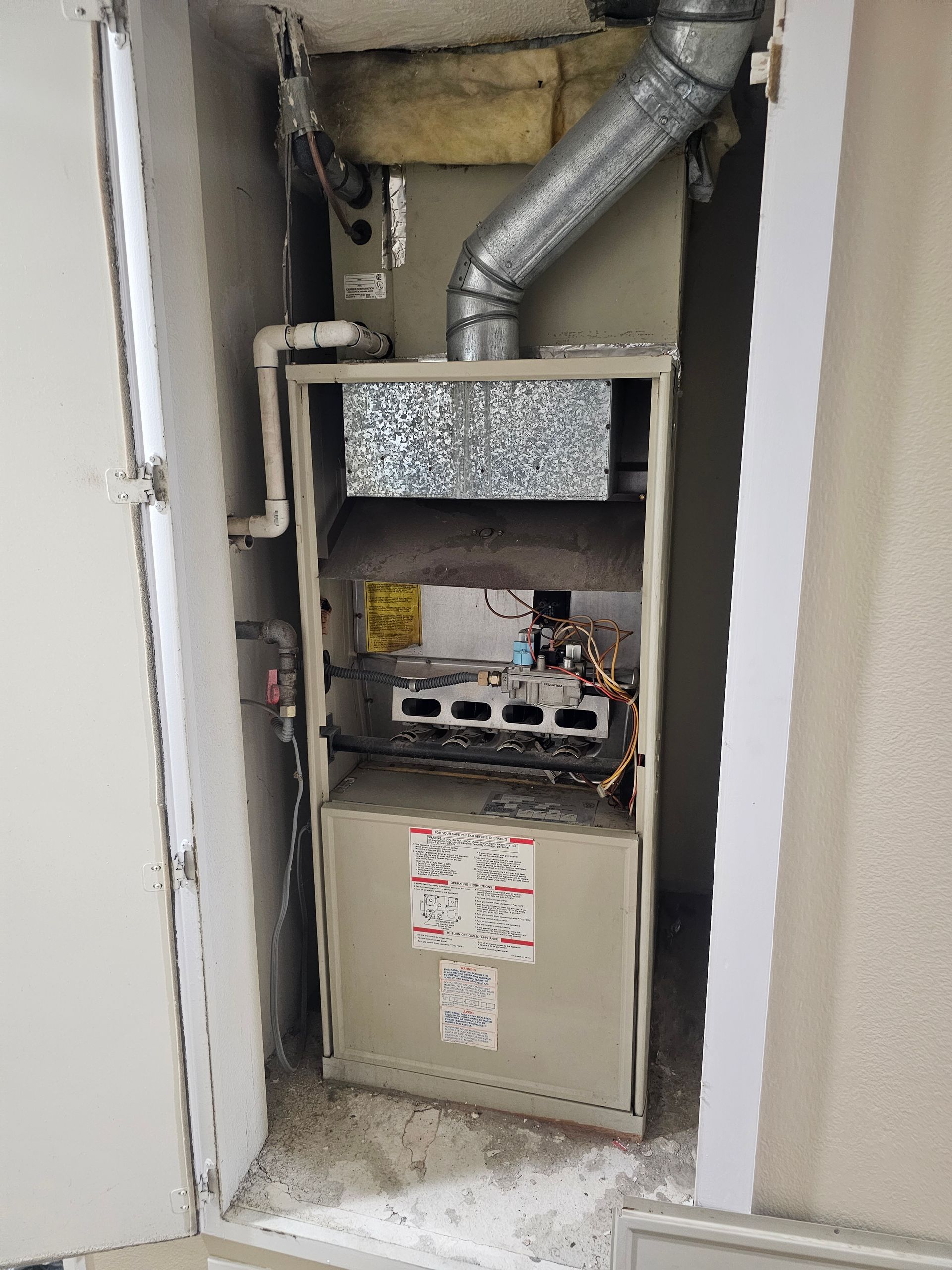 Open furnace closet with exposed HVAC unit, ductwork, and service labels