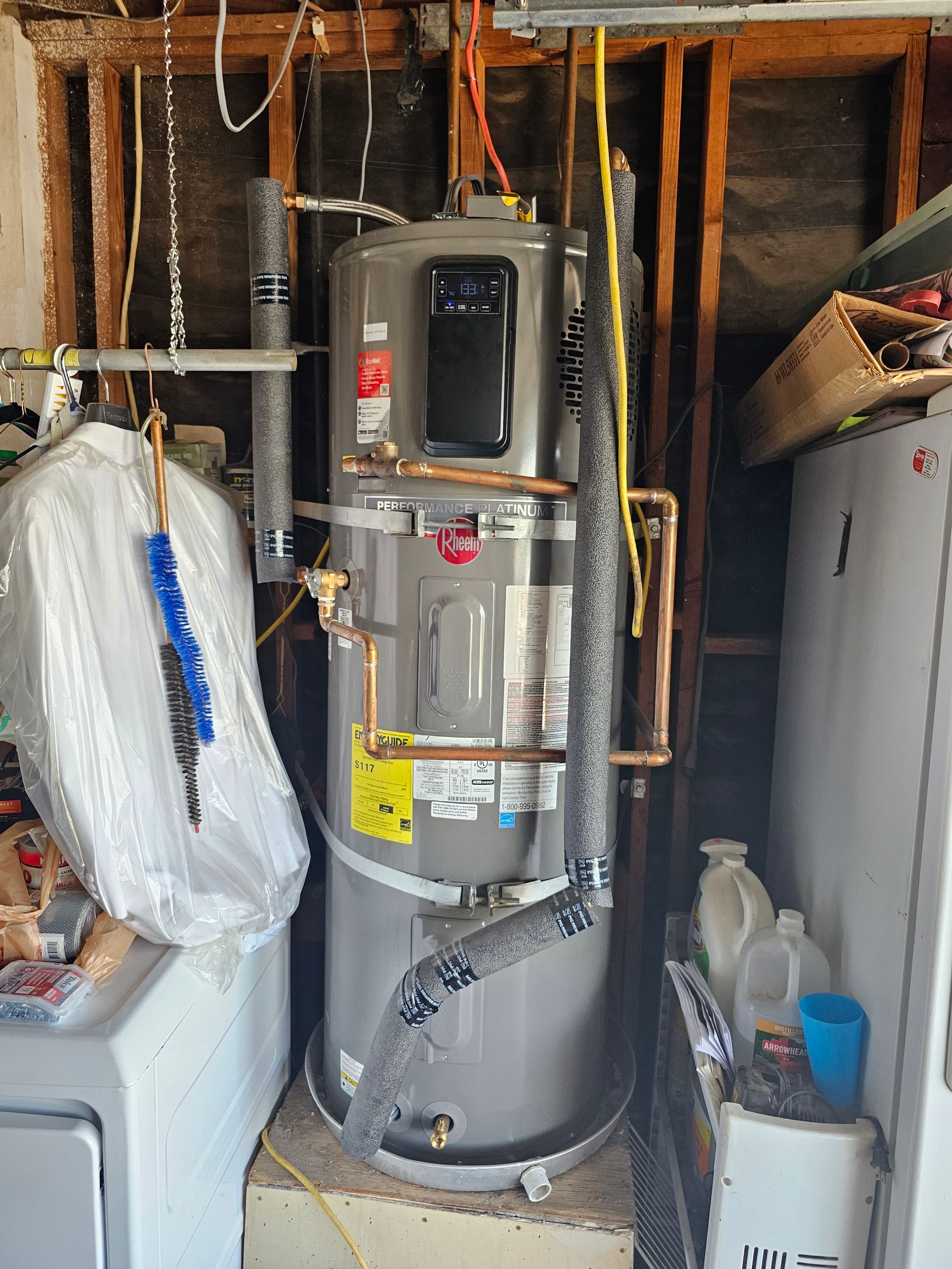 Water heater in a cluttered utility closet with exposed pipes and insulation.