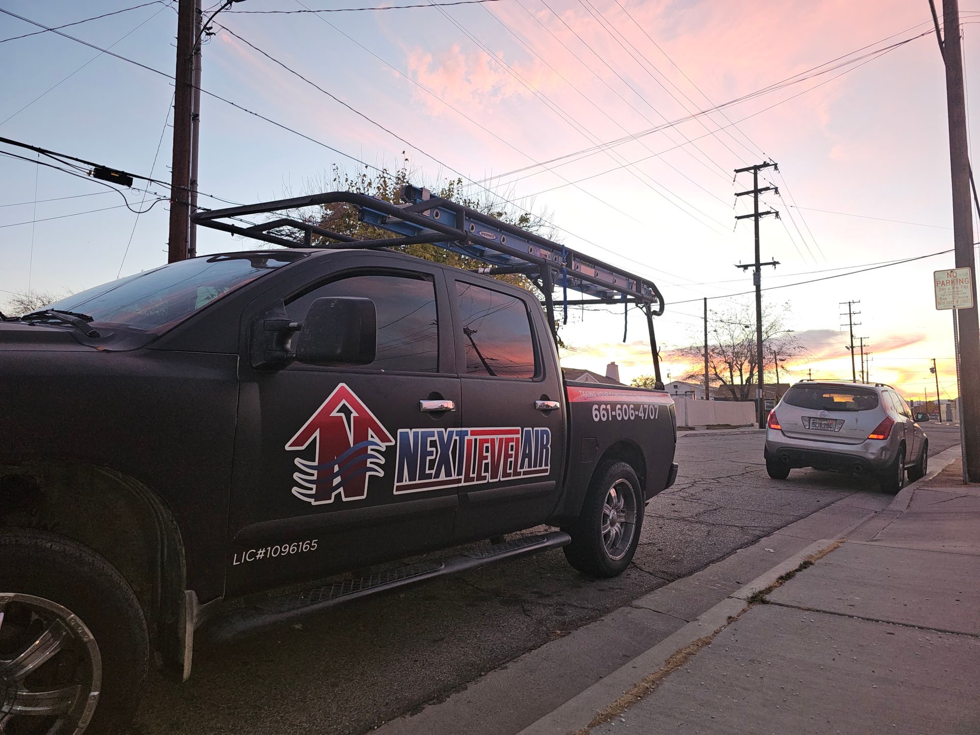 Black pickup truck with a roof rack parked on a street at sunset, with a white car ahead.