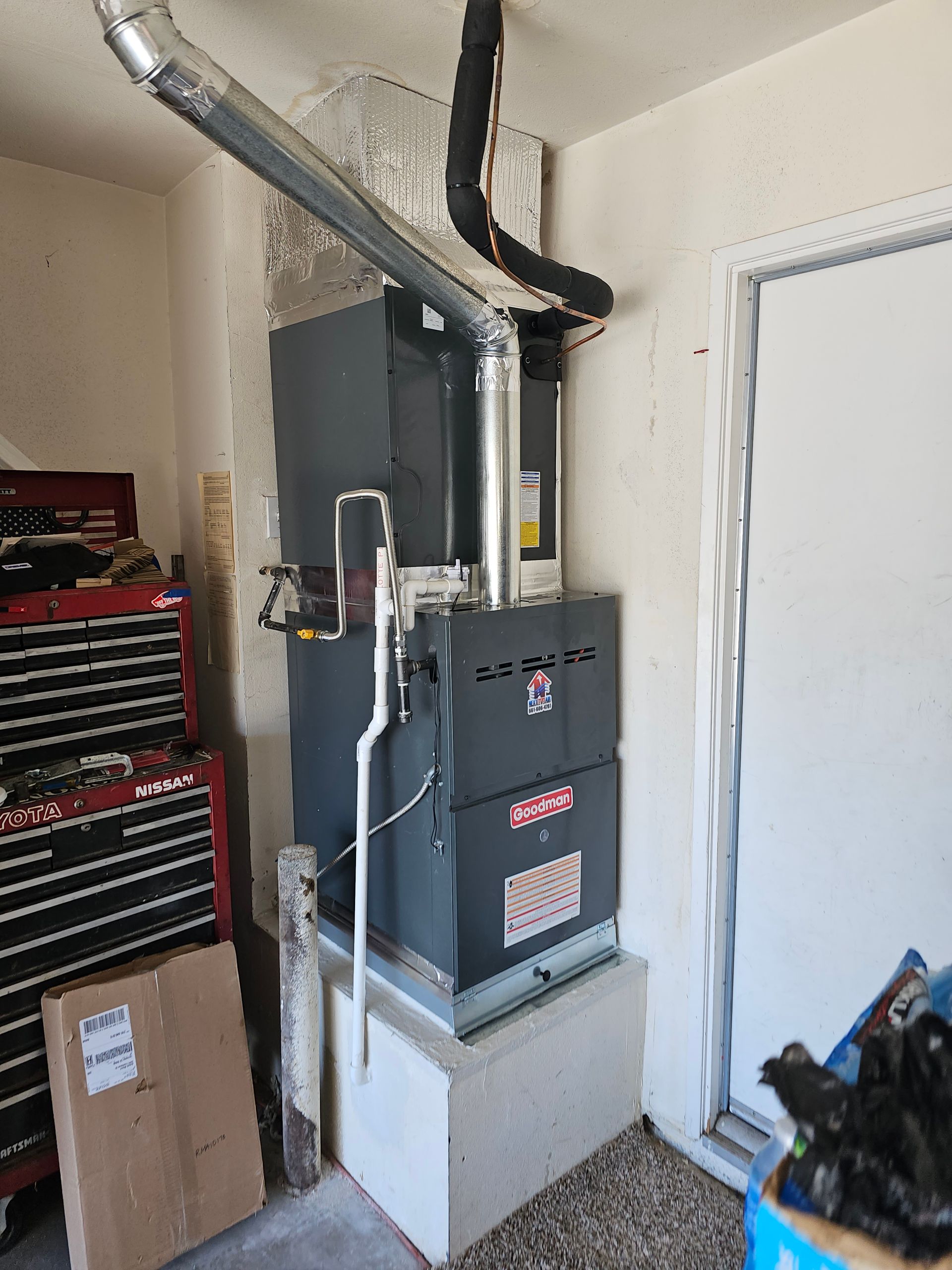 Indoor utility closet with furnace, ductwork, and white door; cardboard box and red tool chest nearby
