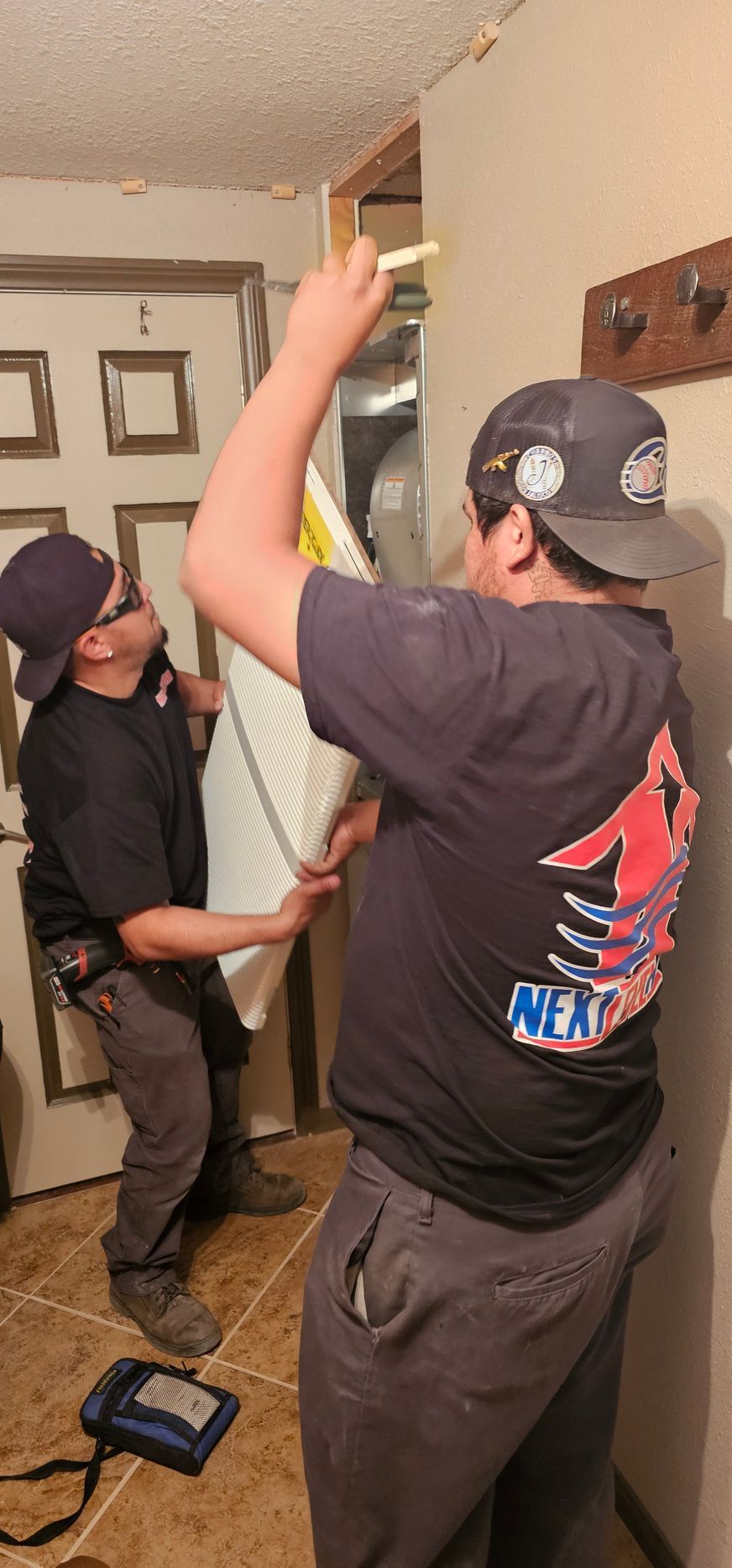 Two people installing a ceiling fixture in a living room, one on a ladder and one holding a tool