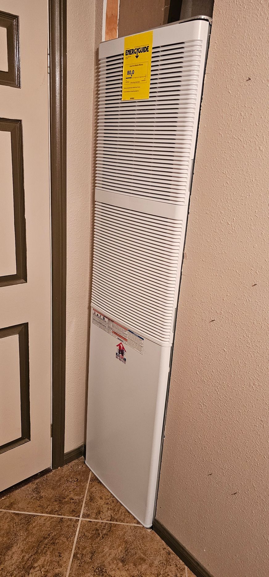 White radiator leaning against a wall in a corner, with a yellow label near the top.