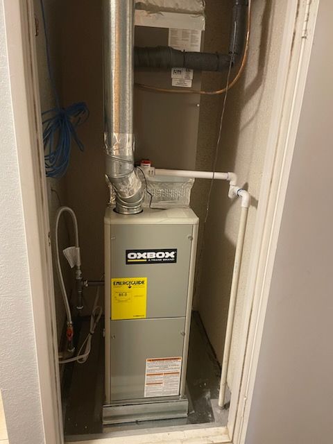 Closet with a gray furnace and exposed ductwork in a narrow utility space