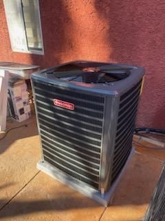 Outdoor air conditioner unit against a red stucco wall in a sunlit patio area