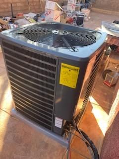 Gray outdoor air conditioner unit with top fan and yellow warning label in a store display area