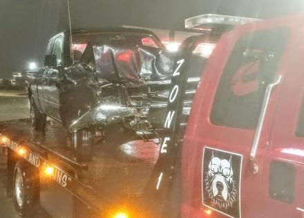 A heavily damaged pickup truck is secured onto the flatbed of a red tow truck at night.