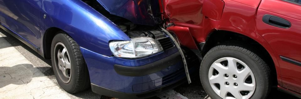 A blue car has crashed into the side of a red car in an outdoor setting.