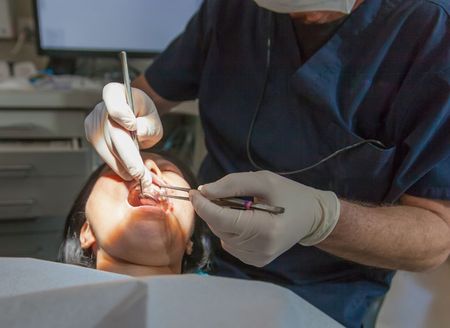 Dentist and assistant examining a patient in a dental clinic, with tools near her open mouth