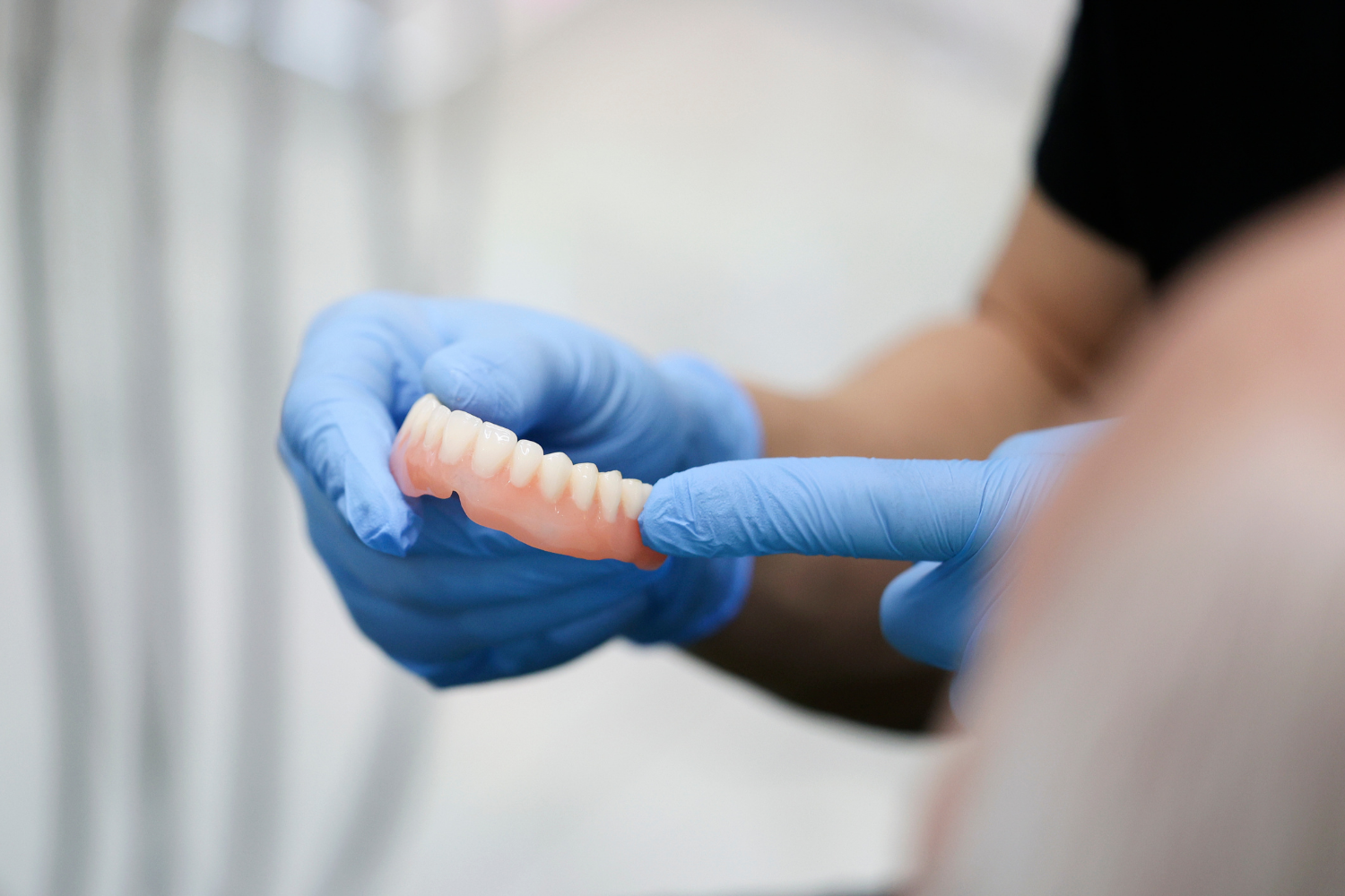 Gloved hands holding a pink dental arch model during a dental exam demonstration