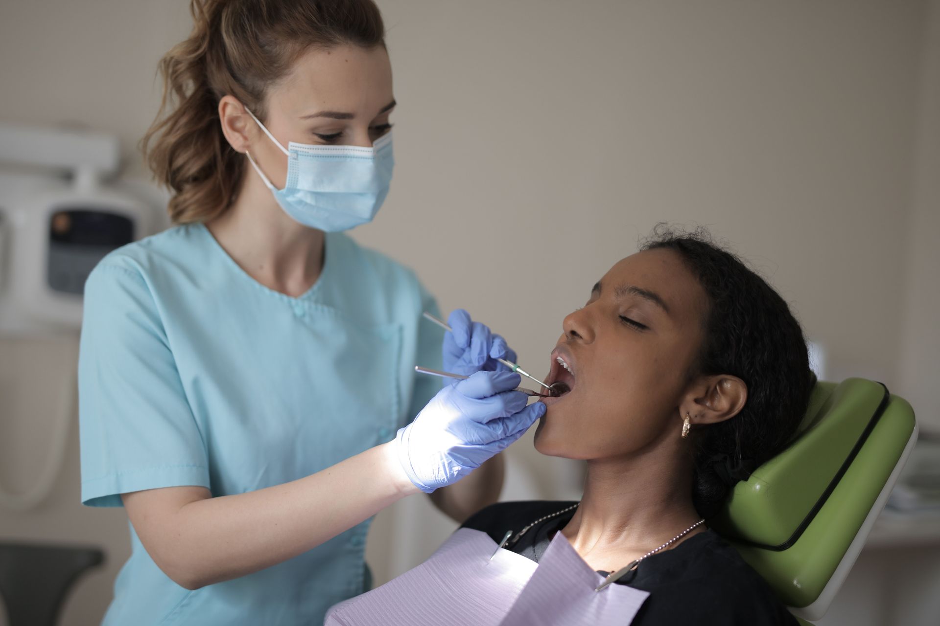 Dentist holding a dental mirror over a patient in a blue bib during an exam