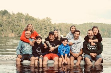 A large family is posing for a picture on a dock in the water.
