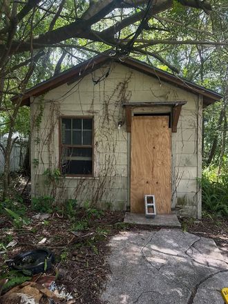 Small weathered shed with boarded door, window, and vines in a wooded yard.