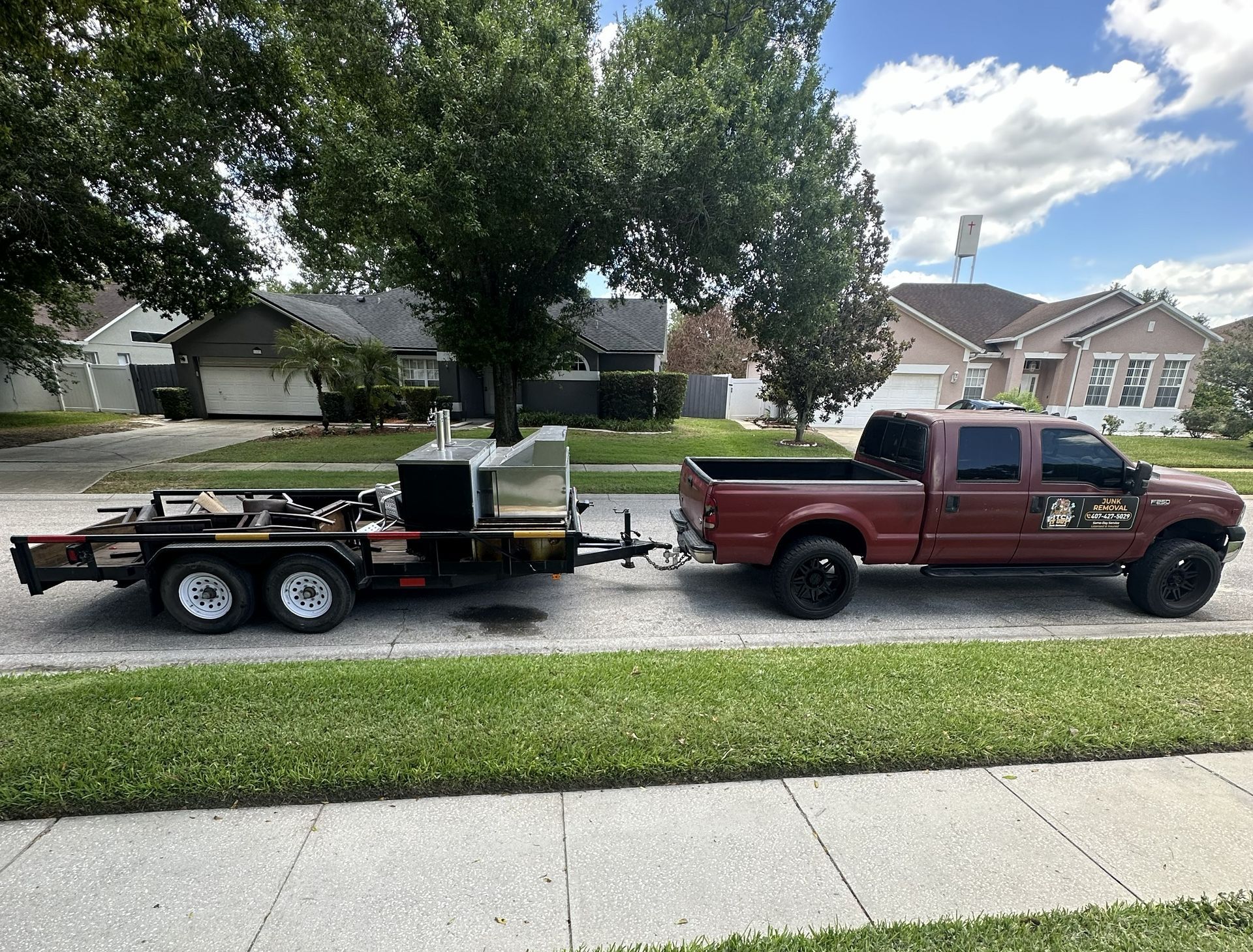 Red pickup truck towing a flatbed trailer with equipment on a suburban street.