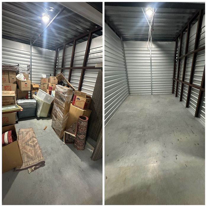 Storage unit interior: cluttered boxes and goods on left, empty concrete floor and metal walls on right.