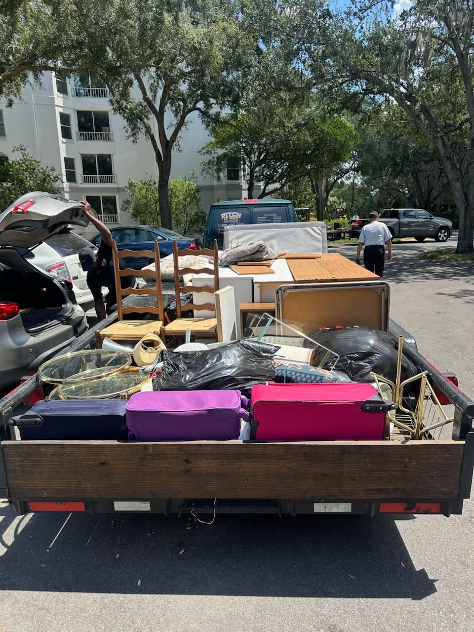Pickup truck loaded with furniture and boxes on a street, with trees and apartment buildings in the background