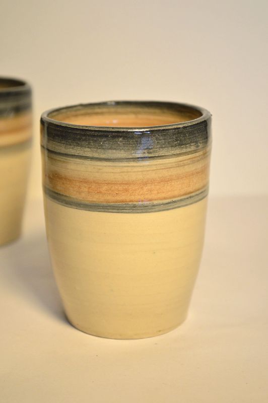 Handen die een kleipot vormgeven op een pottenbakkerswiel, met natte klei en een draaiend wiel.