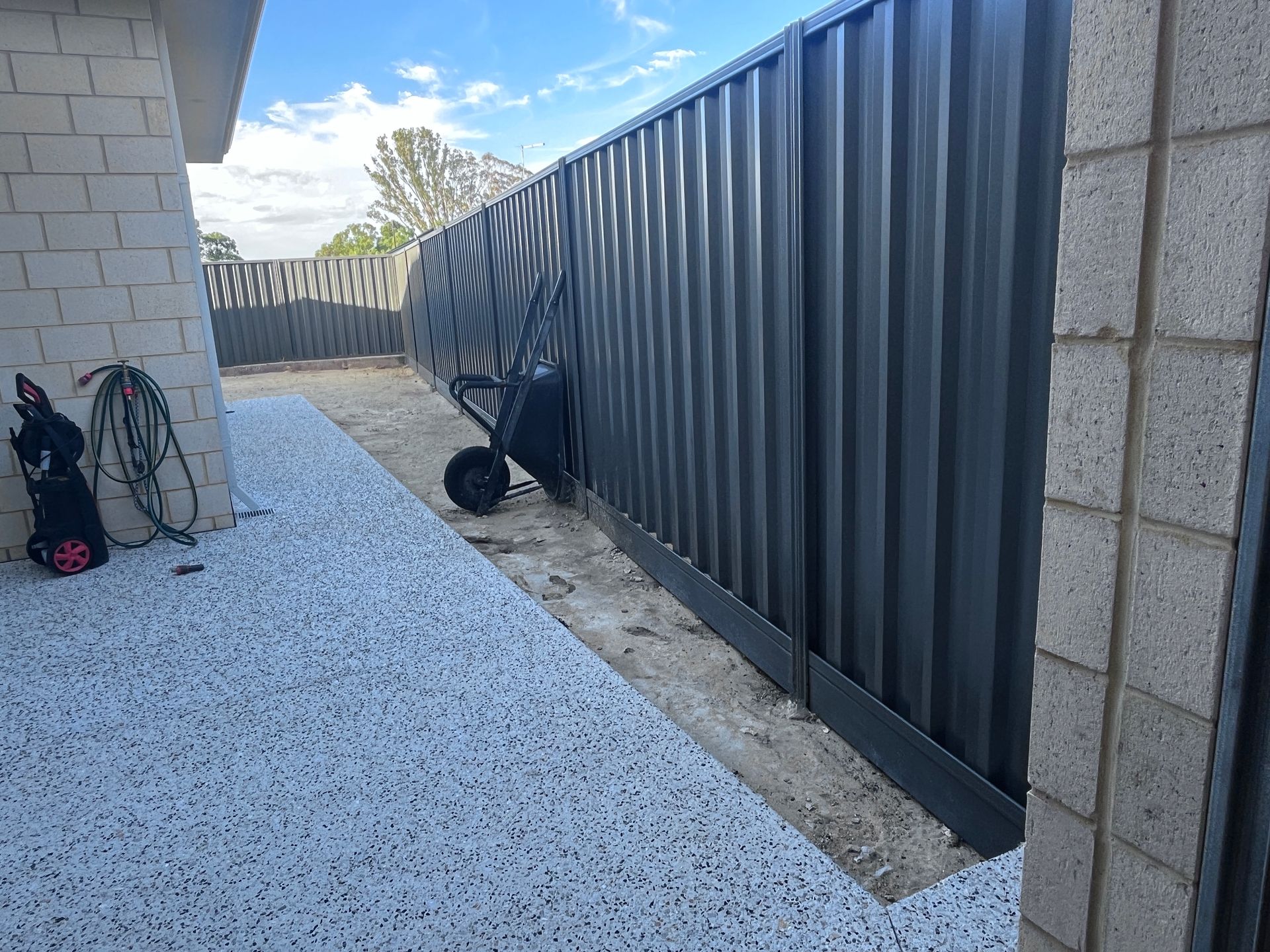 Backyard with gray fence, gravel, concrete, and a wheelbarrow.