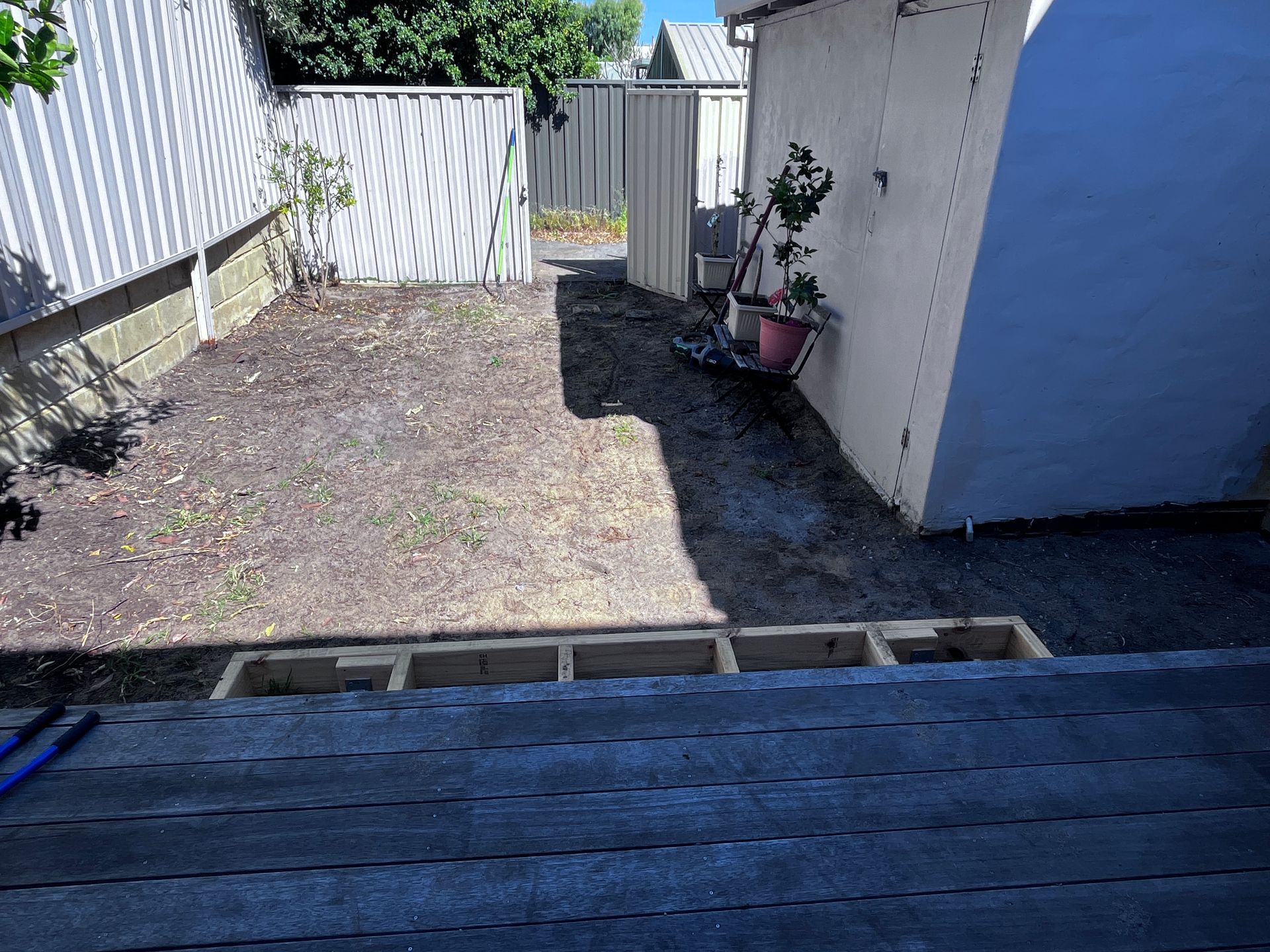 Backyard with bare soil, wooden frame, and fences. A structure stands on the right.