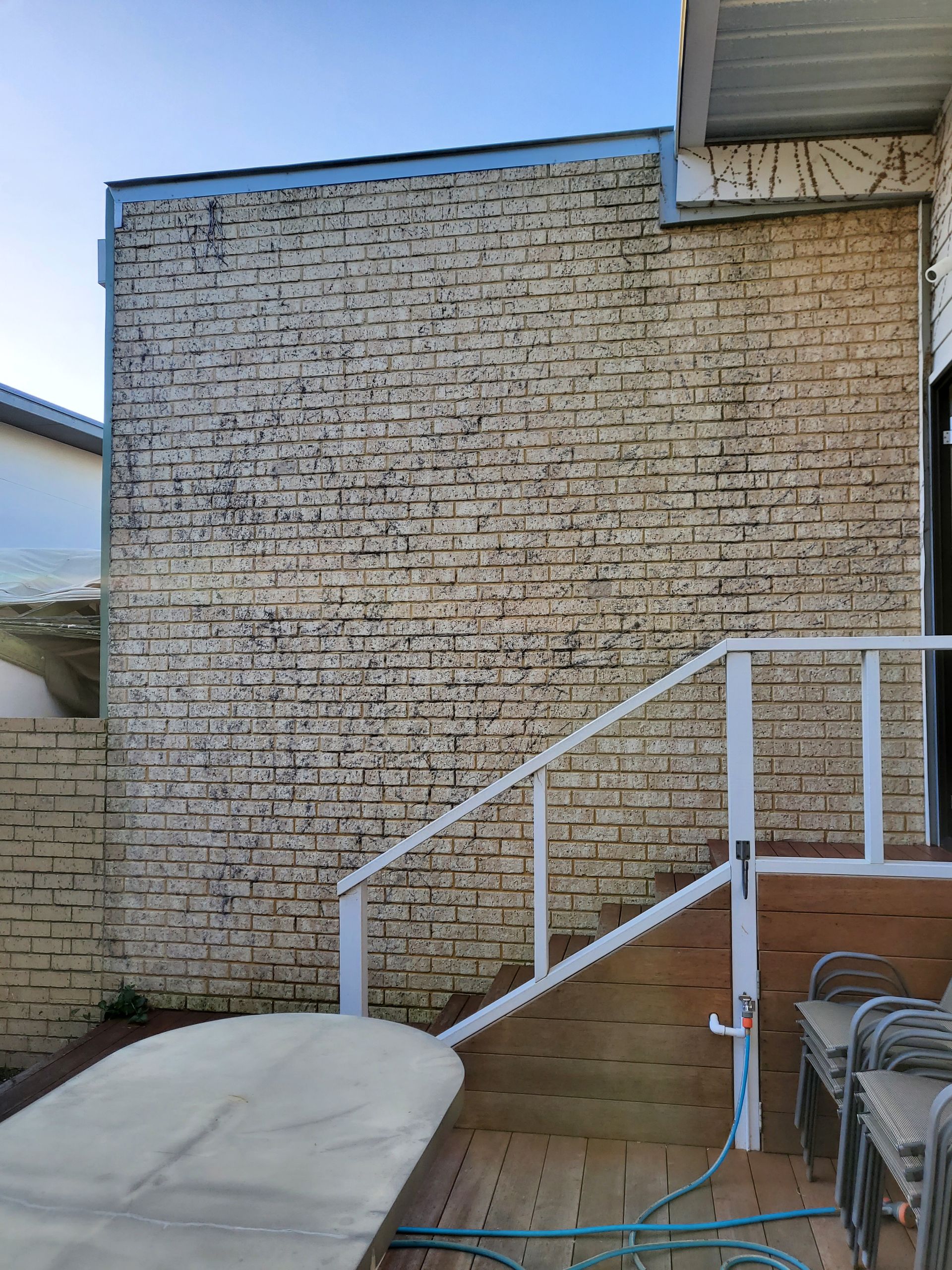 Brick-patterned exterior wall with a white railing and wooden deck. Blue sky in background.