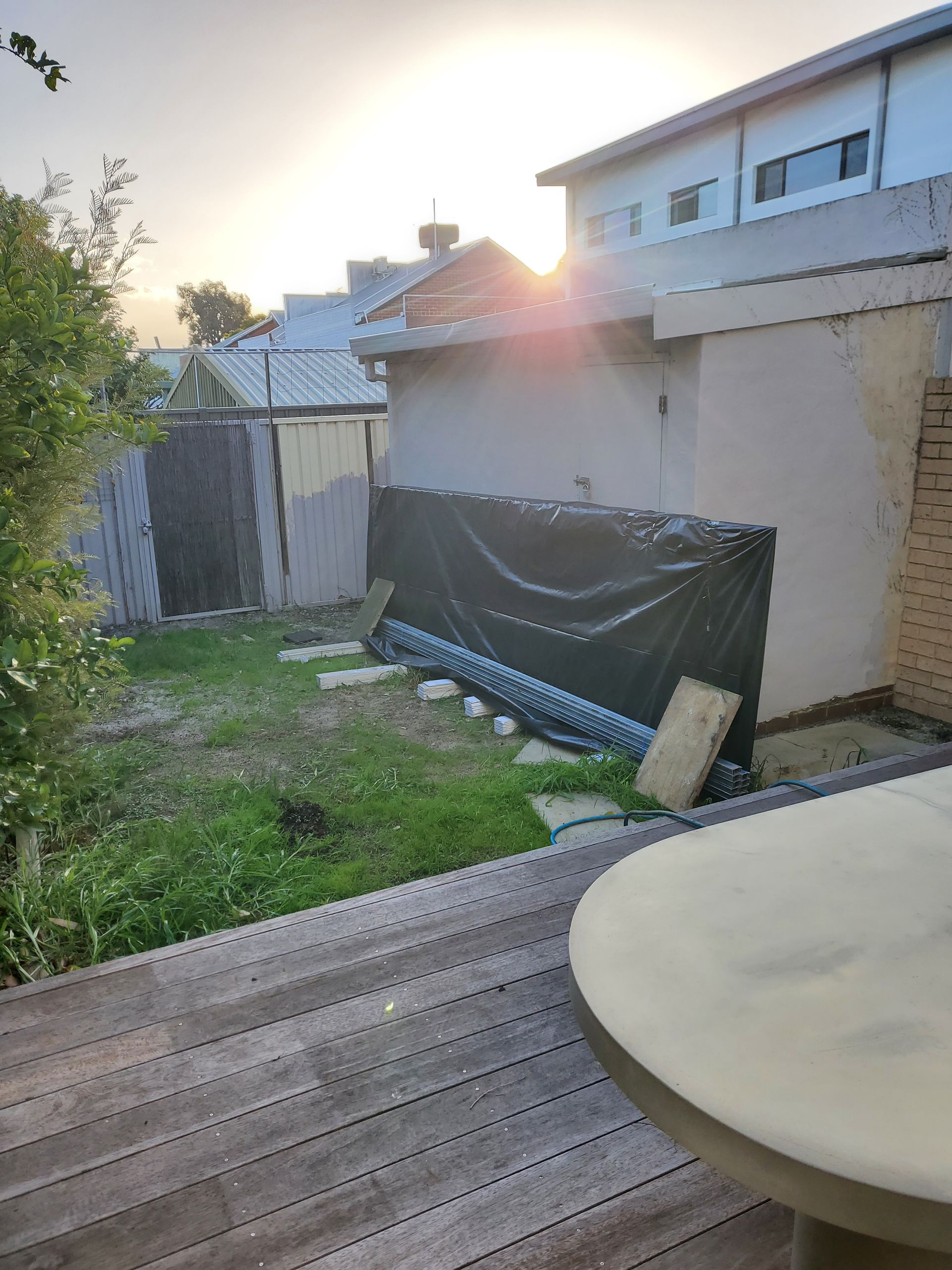 Backyard scene: a wooden deck, small shed, and grassy area, with the sun setting in the background.