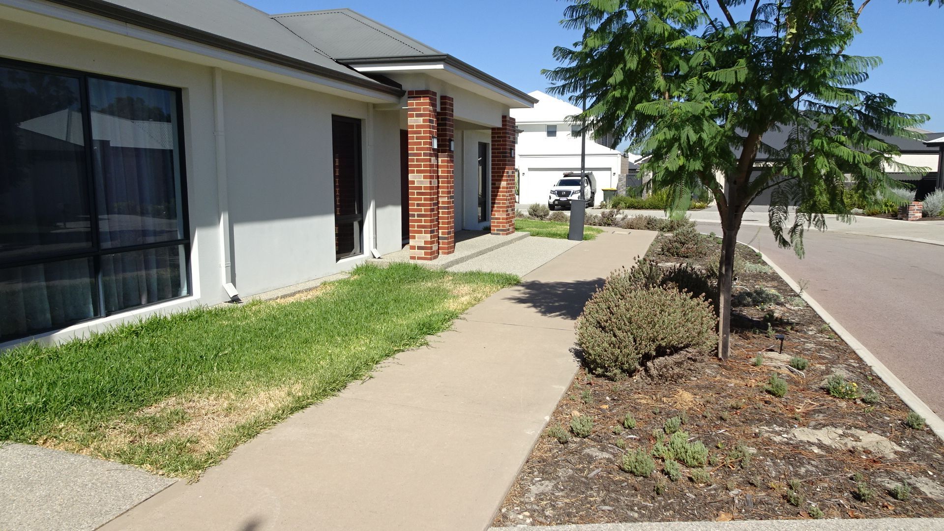 Sidewalk leading to a house with a brick pillar, next to a grassy area and a tree.