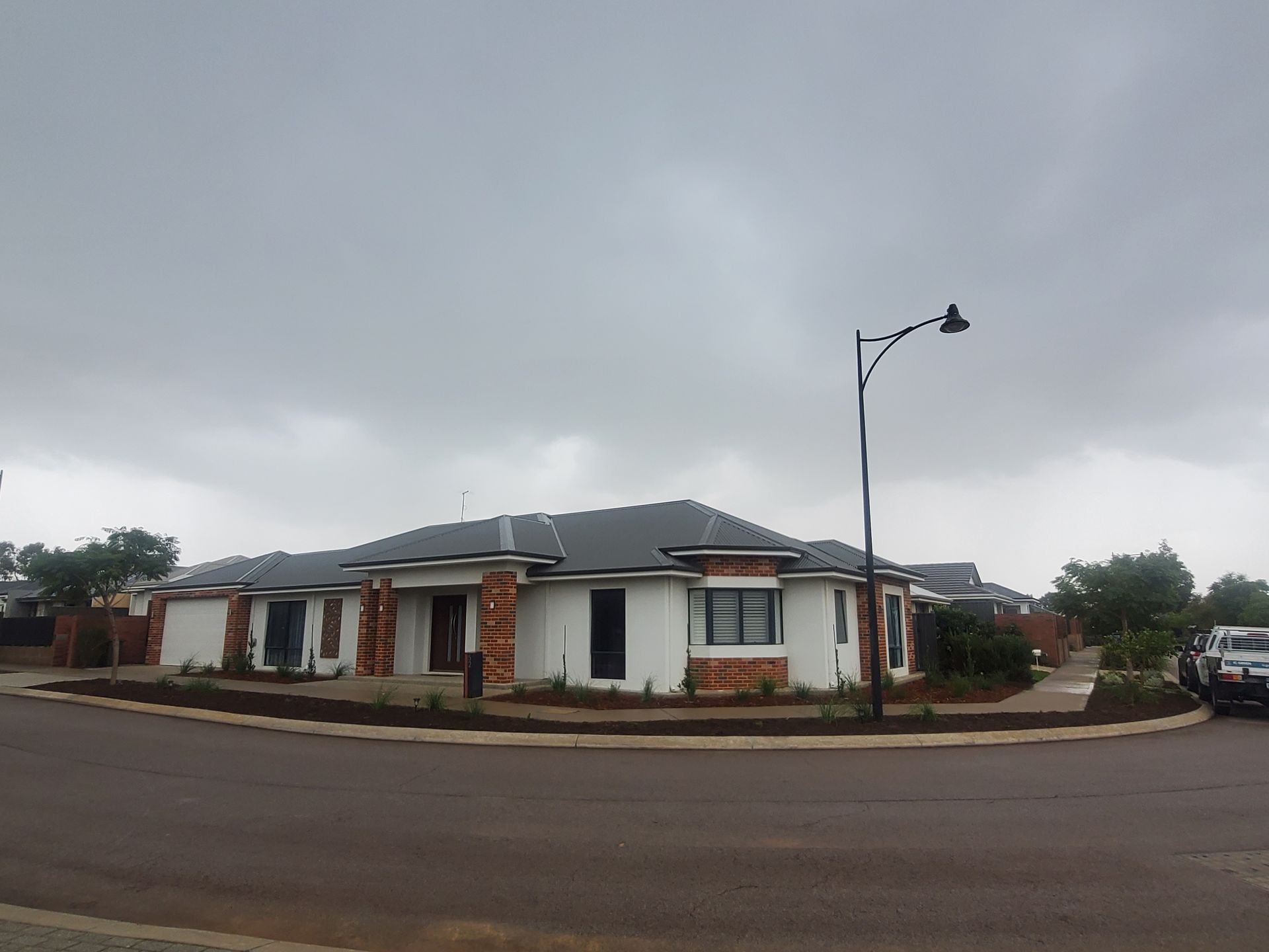 A white house with brick accents on a street corner under a cloudy sky.