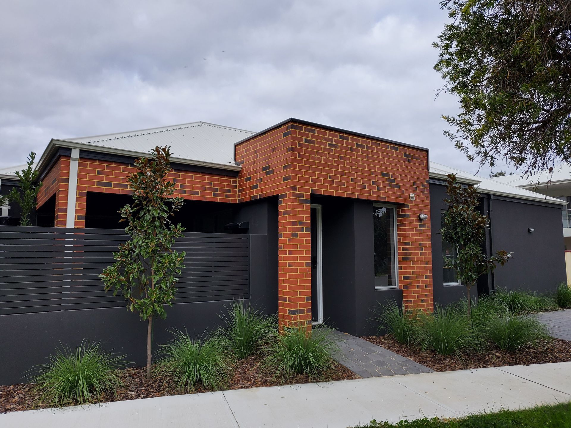 Modern brick and dark gray house with a gray roof and decorative plants.