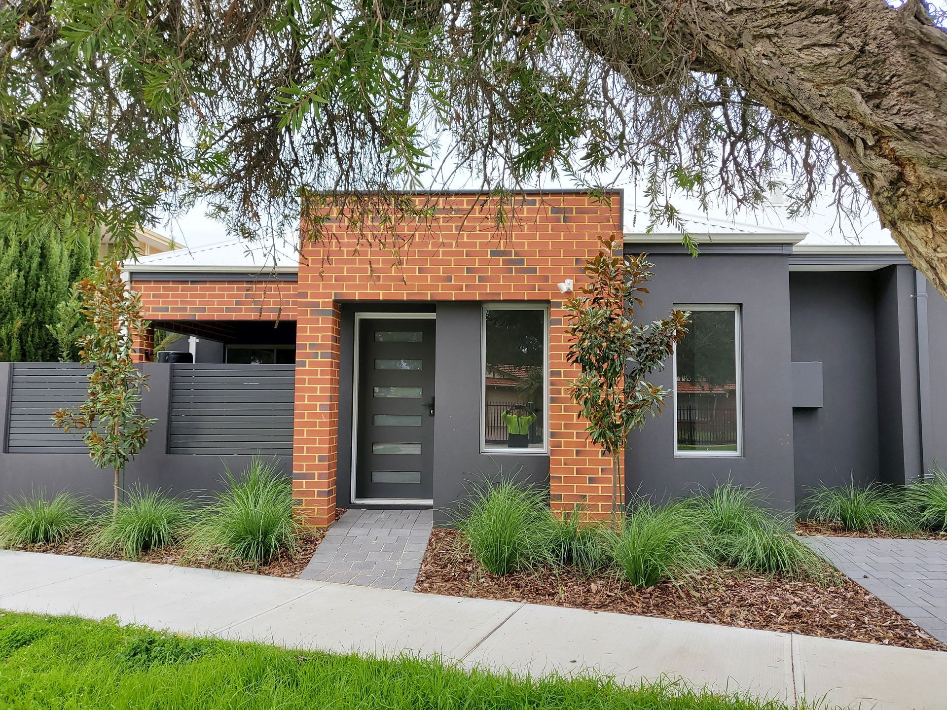 Modern house with brick facade entrance, gray siding, two windows, and small landscaping.