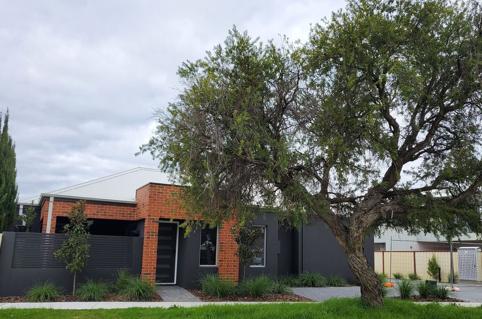 Modern house with brick and dark siding, a large tree, and a cloudy sky.