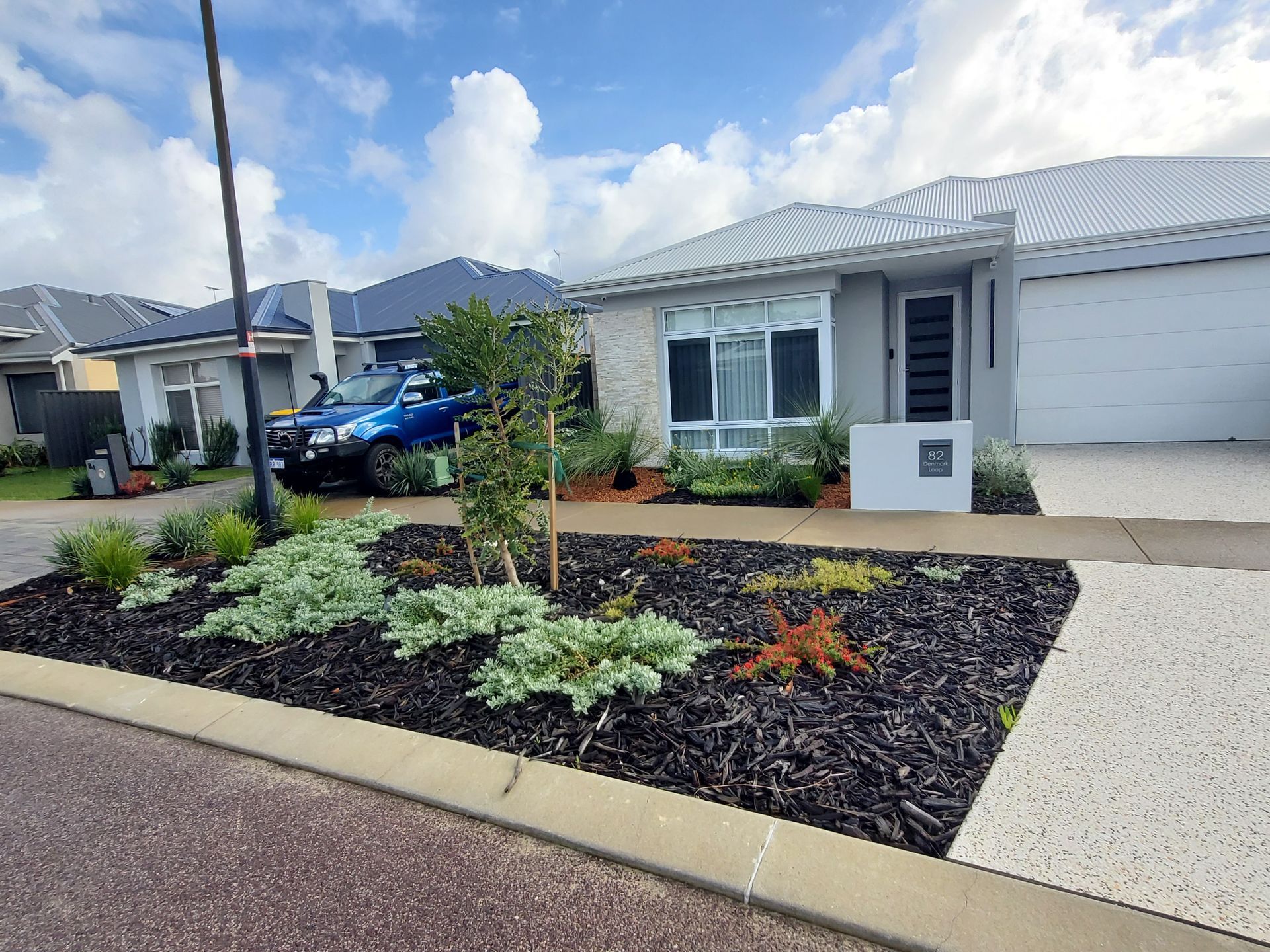 Modern house with landscaped front yard, black mulch, small tree, and a police vehicle parked in the street.