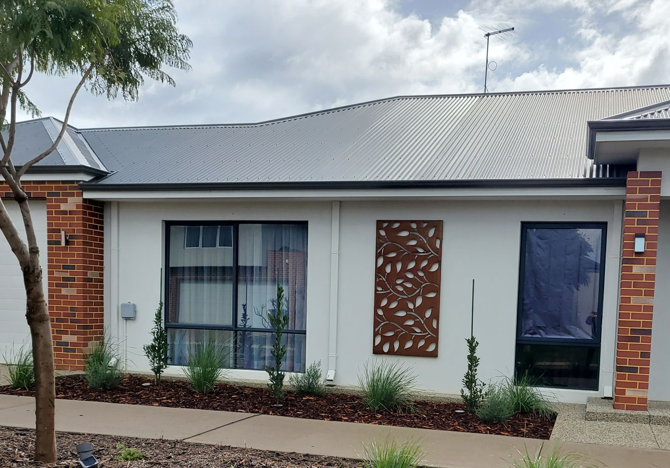 Modern house exterior with white walls, black-framed windows, brick accents, and a metal roof against a cloudy sky.