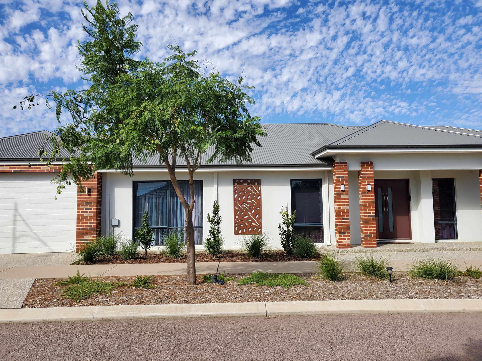 Single-story home with red brick accents, light walls, and a small tree in front under a blue sky.