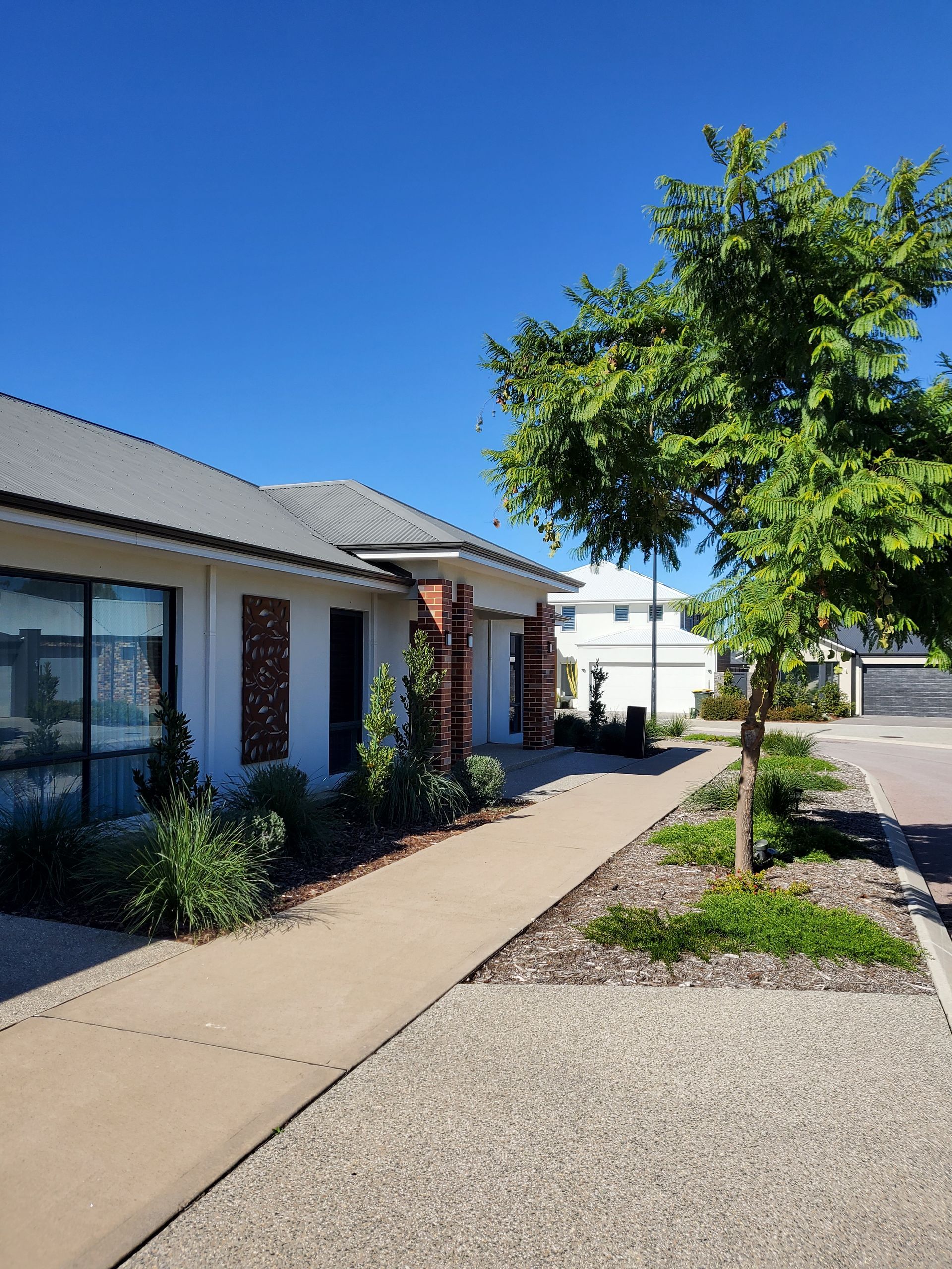 Modern single-story house exterior with walkway, desert landscaping, and blue sky