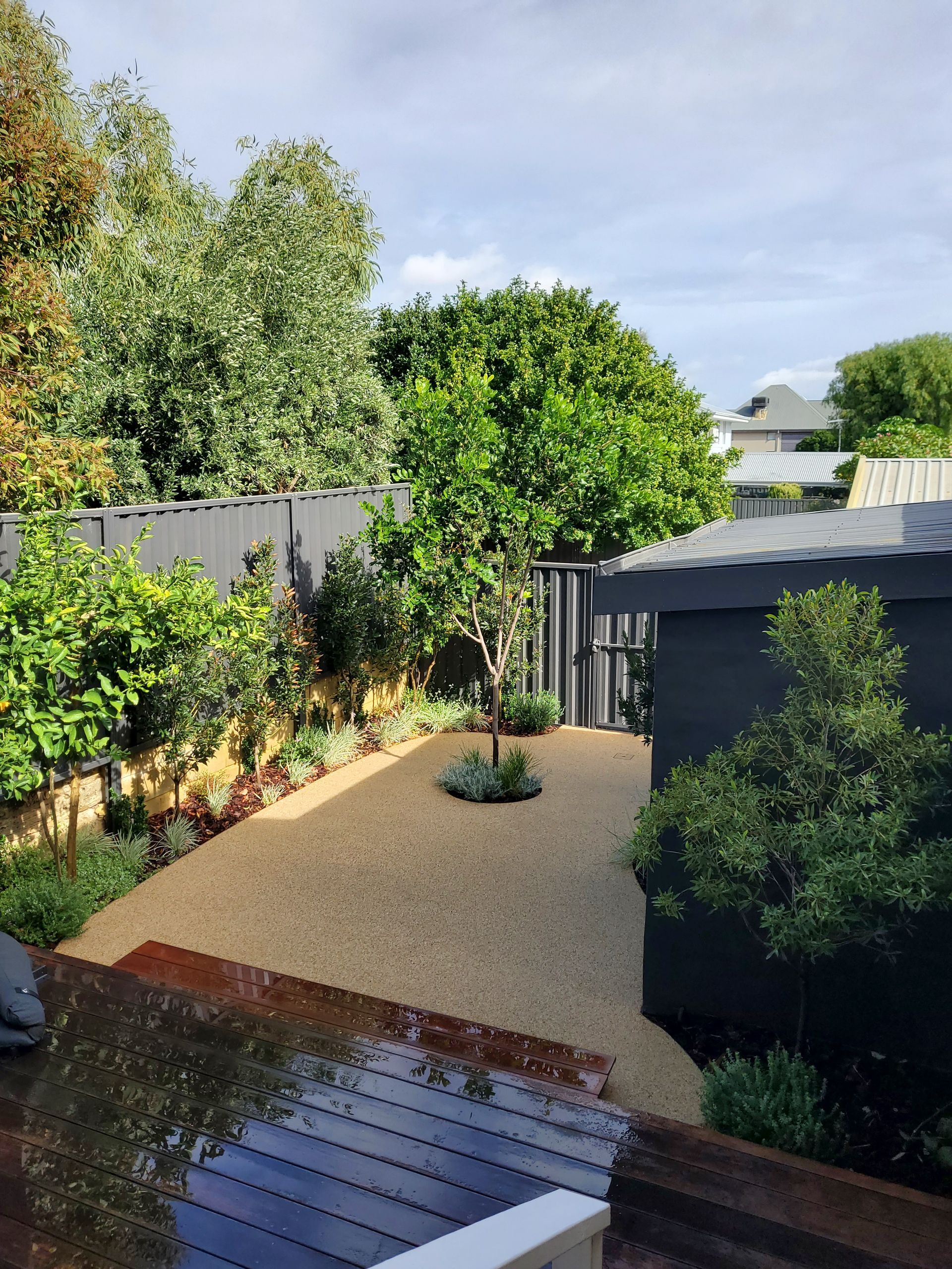 Backyard patio with gravel courtyard, trees, shrubs, and a small shed under a bright sky