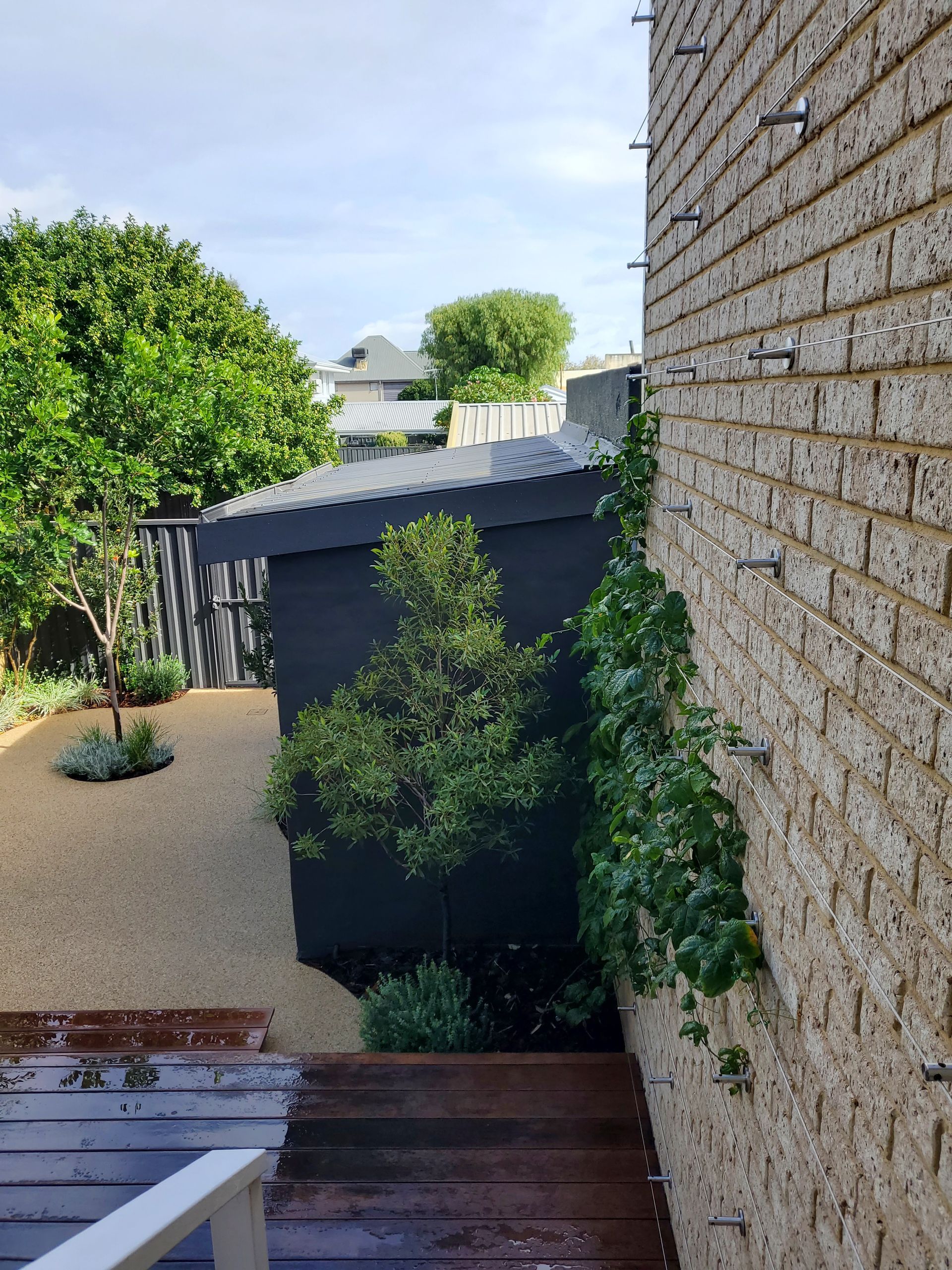 Backyard patio with wooden steps, gravel yard, trees, and a brick house wall with vines