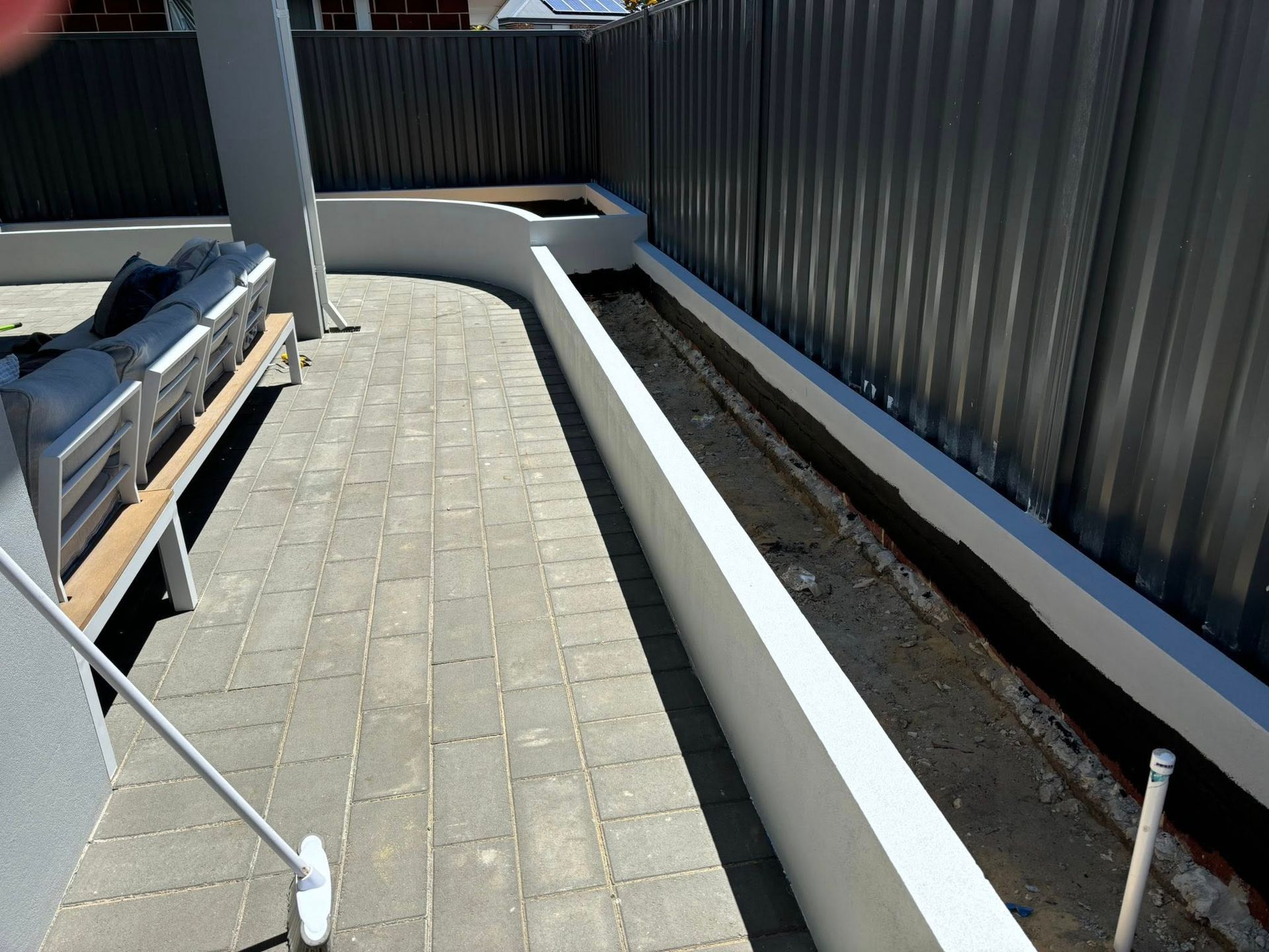 A paved outdoor area with a long planter box, a fence, and a bench.
