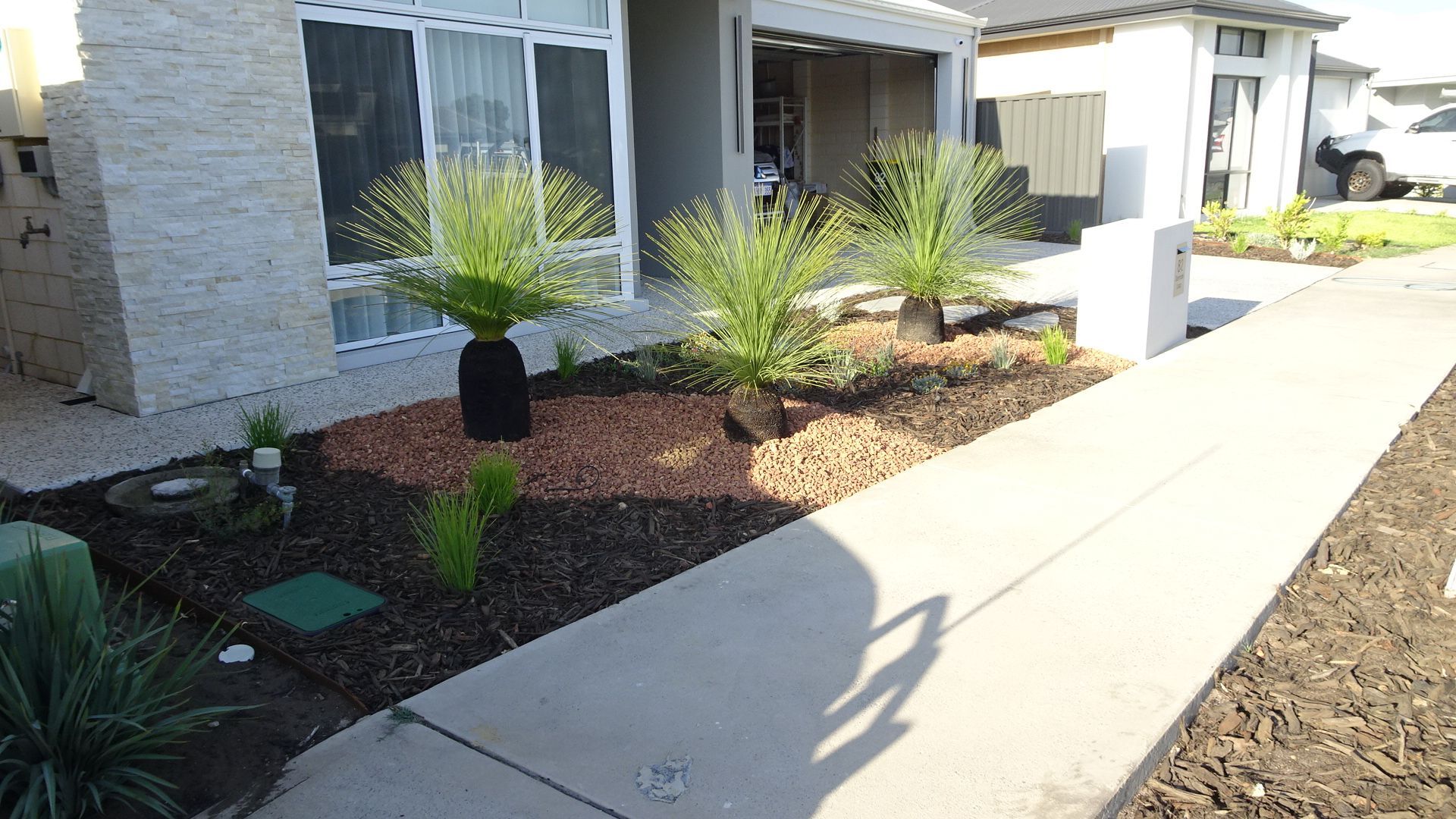 A house exterior with a sidewalk, flower bed, and several green plants in front.