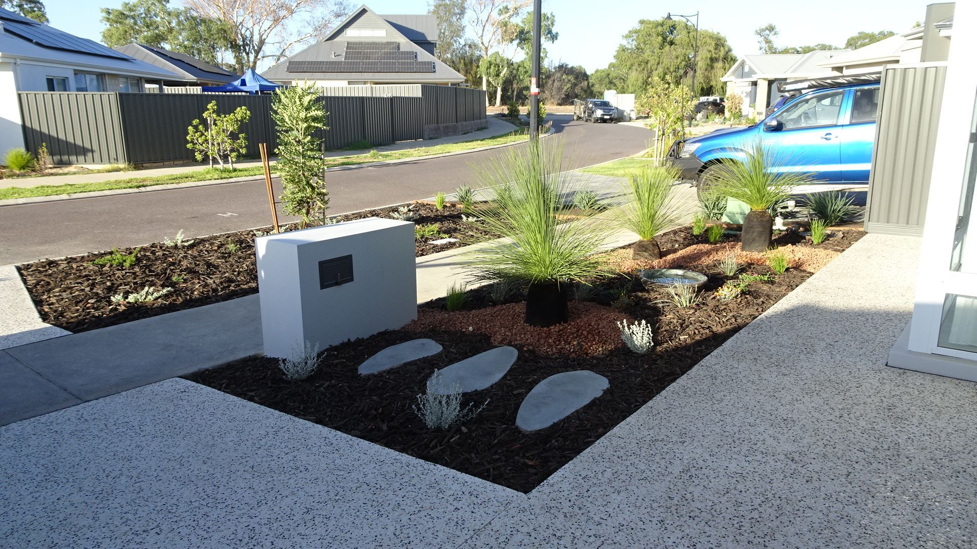 Front yard landscaping with a mailbox, stepping stones, plants, and a street in the background.