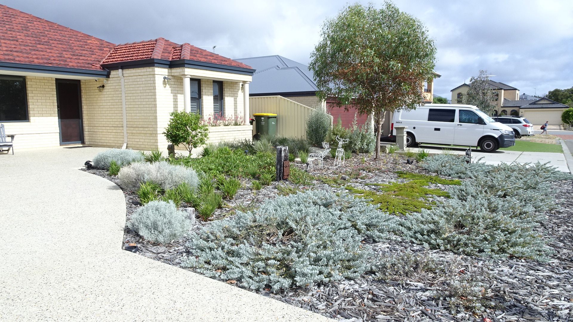 House with landscaped yard, stone path, and parked vehicles.