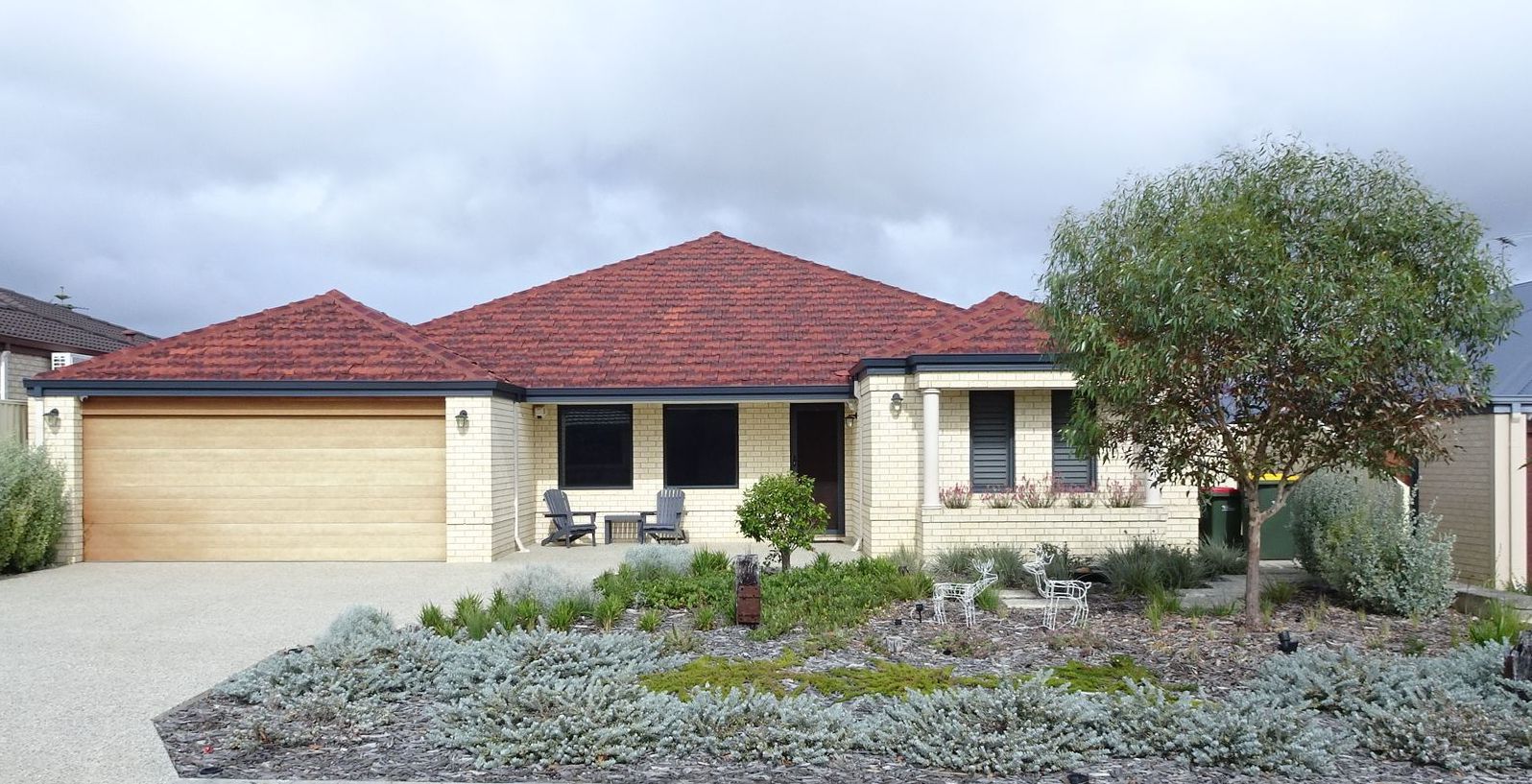 Suburban home with brick facade, red tiled roof, and a gravel driveway. Landscaped garden.