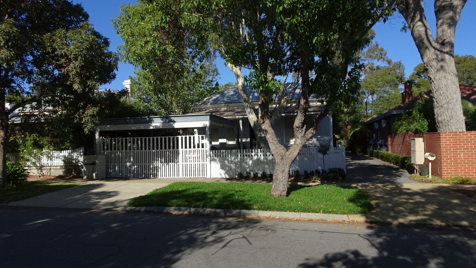 Residential house with a white fence, surrounded by green trees and grass on a sunny day.